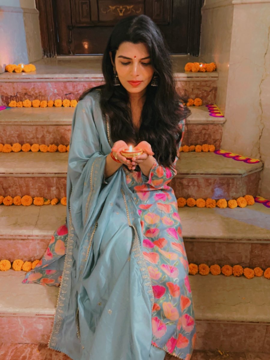 Dr. Nidhi Sharma holding a lit diya on the marigold-lined steps at Diwali